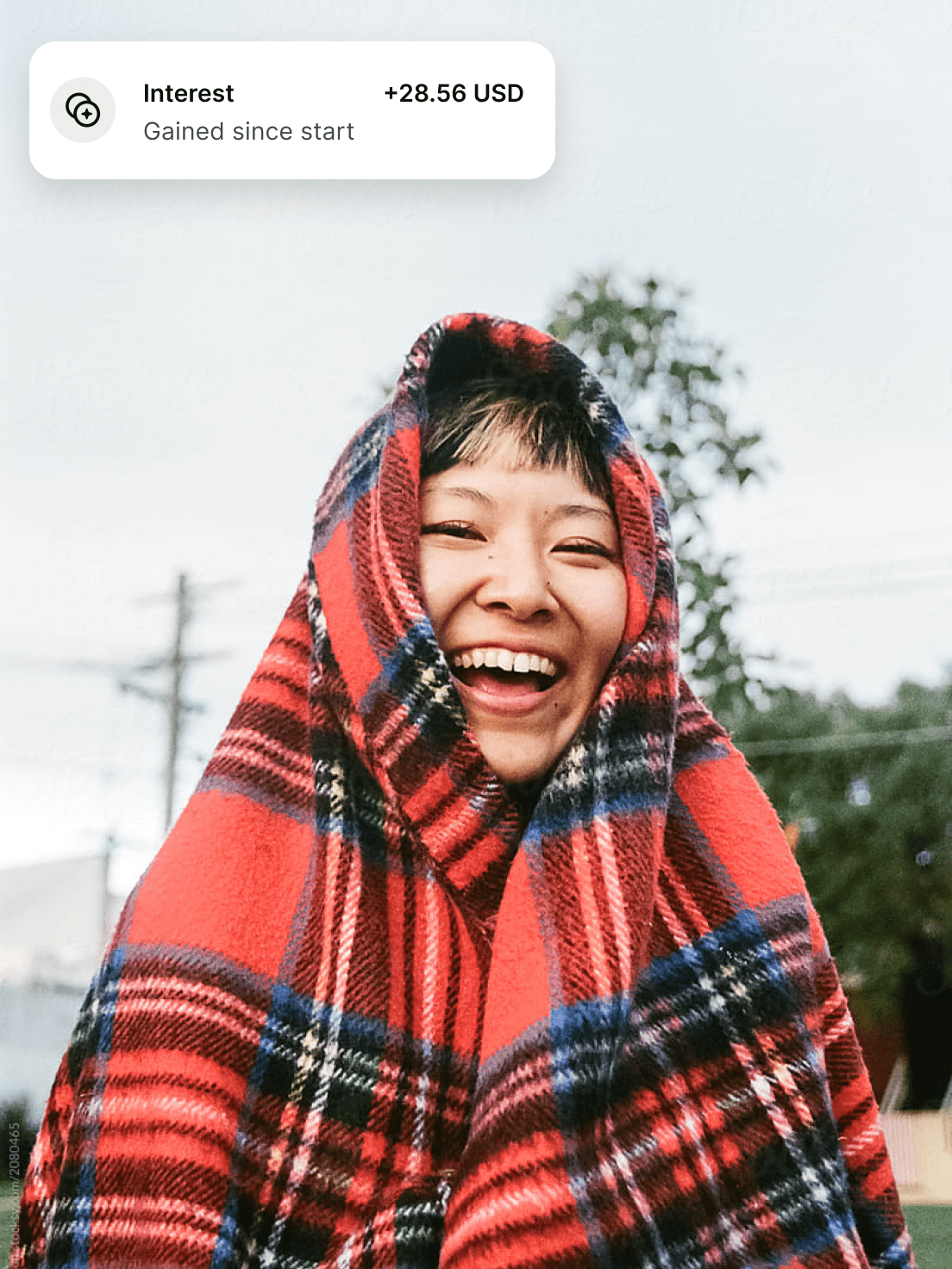 A smiling woman wrapped in a tartan blanket enjoying $28.56 dollars gained since start