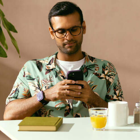 カフェのテーブルに座り、スマートフォンアプリを使ってWiseアカウントを確認している男性。